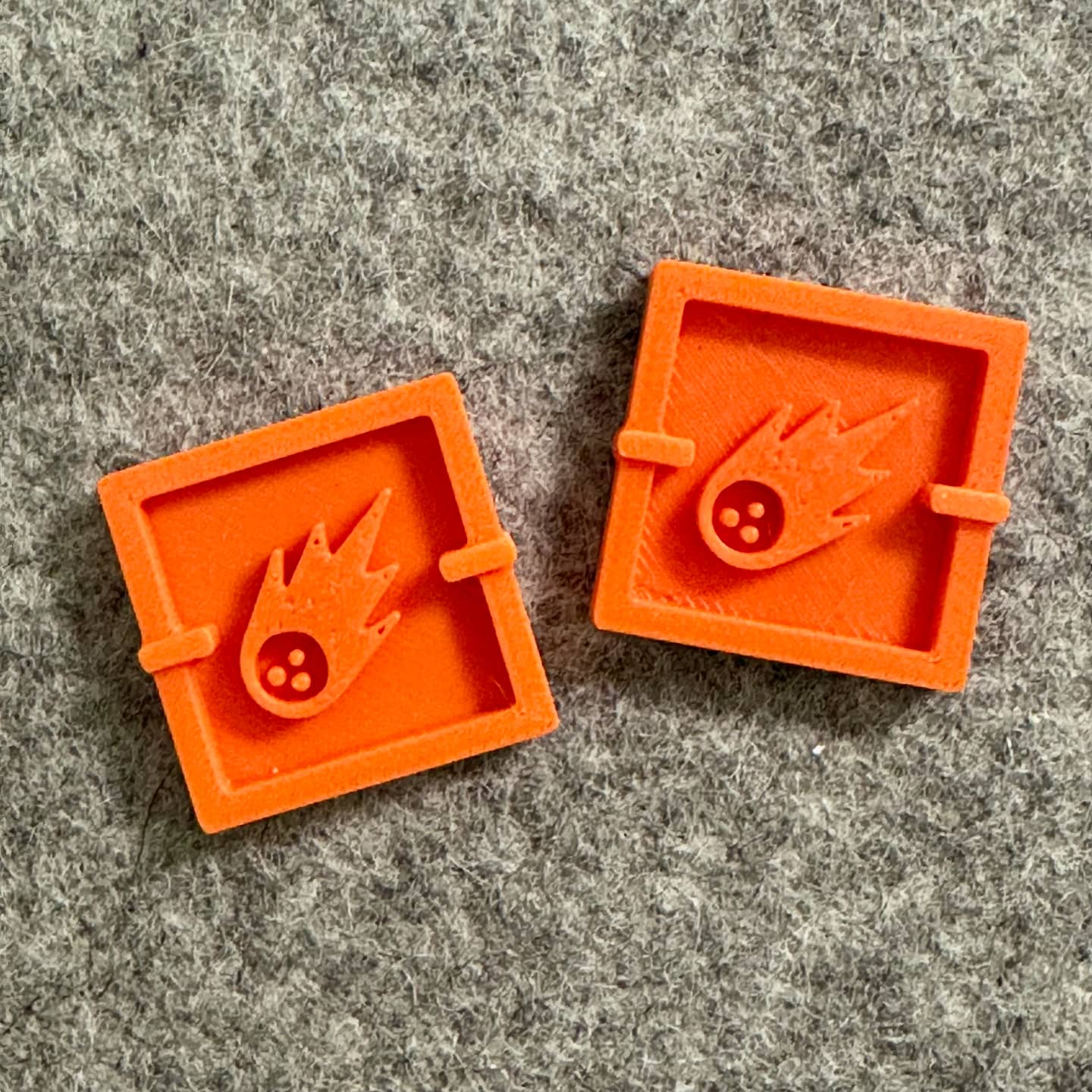 Two orange square-shaped objects with a design on a gray textured surface