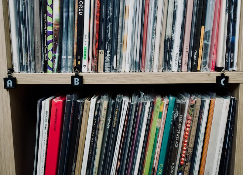 Vinyl records on a white oak Ikea shelf. Vinyl is organized alphabetically and labeled with black shelf tags for the letters A, B, and C.