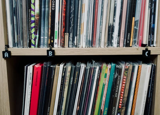 Vinyl records on a white oak Ikea shelf. Vinyl is organized alphabetically and labeled with black shelf tags for the letters A, B, and C.