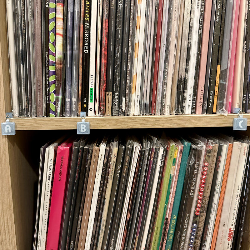 3D-printed letter tags shown in transparent blue on a shelf storing vinyl records.
