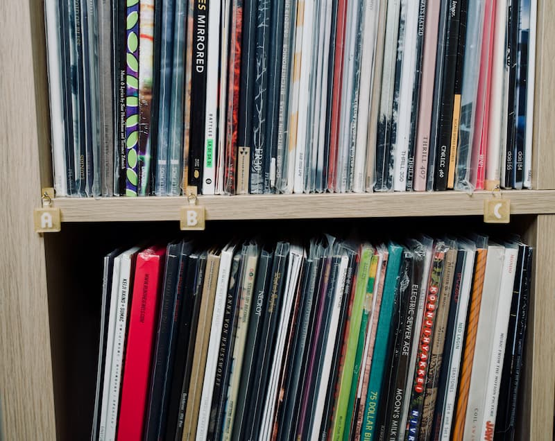 Vinyl records on a white oak Ikea shelf. Vinyl is organized alphabetically and labeled with light gold shelf tags for the letters A, B, and C.