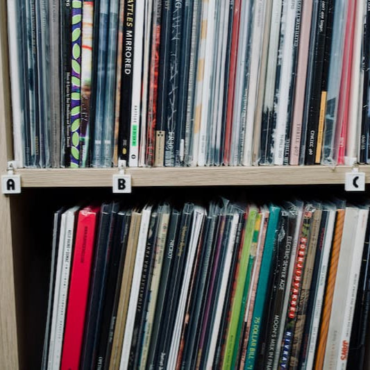Vinyl records on a white oak Ikea shelf. Vinyl is organized alphabetically and labeled with white shelf tags for the letters A, B, and C.